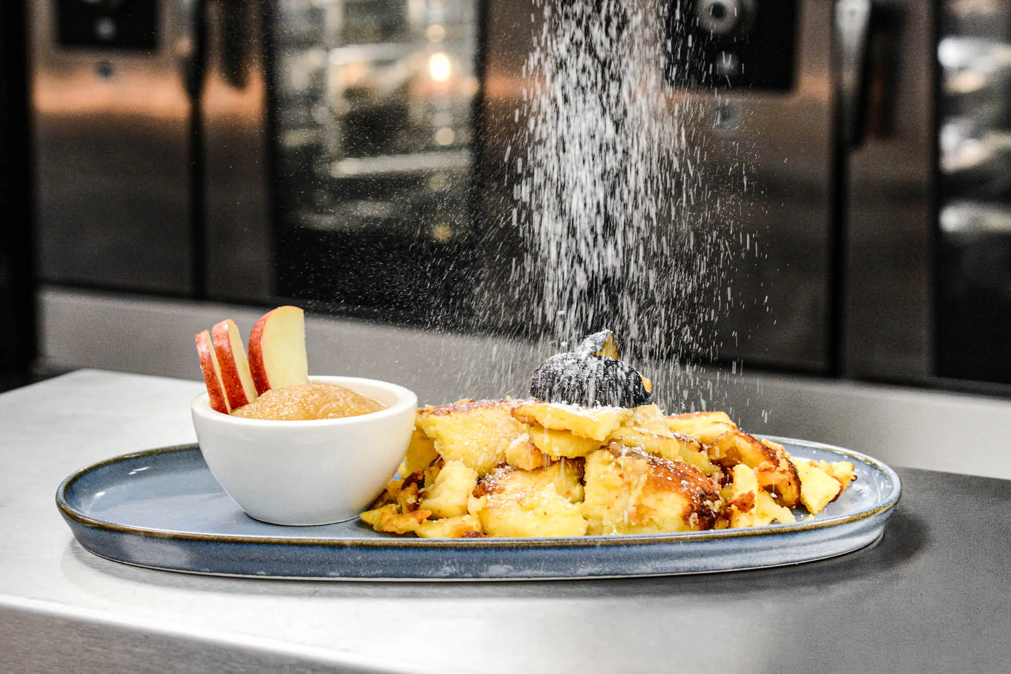 Kaiserschmarrn wird in der Küche mit Staubzucker bestreut, daneben Apfelmus